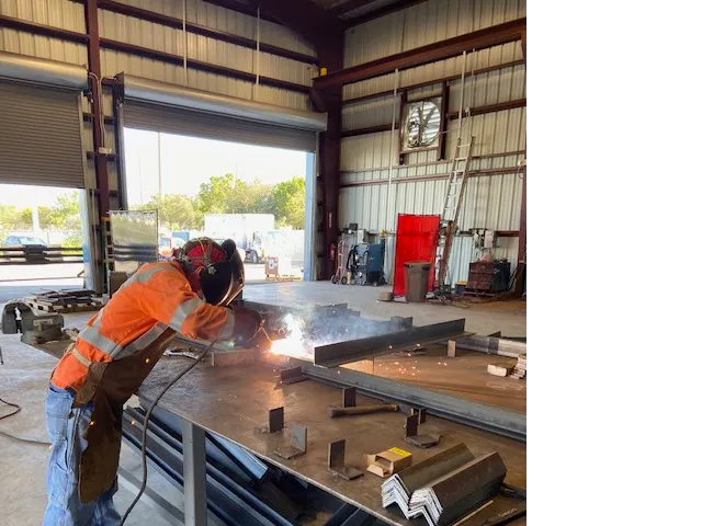 TL Welding fabricator MIG welding a custom steel assembly inside the Medley shop